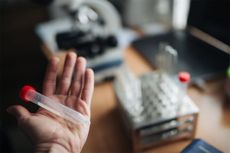 Provetta sterile nella mano di un operatore, davanti al microscopio del laboratorio